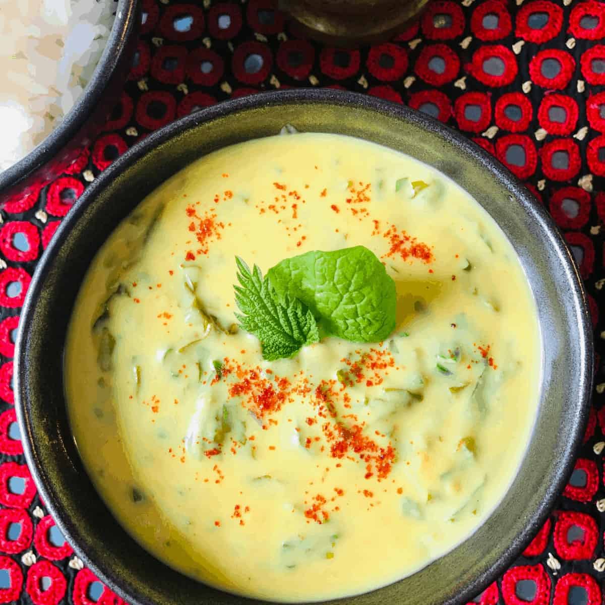 Overhead photography of a bowl of Kadhi garnished with mint nettle and Spinach leafs