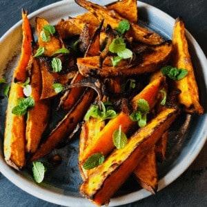 A plate of spiced roasted sweet potato wedges garnished with mint leaves