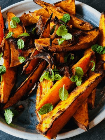 A plate of spiced roasted sweet potato wedges garnished with mint leaves