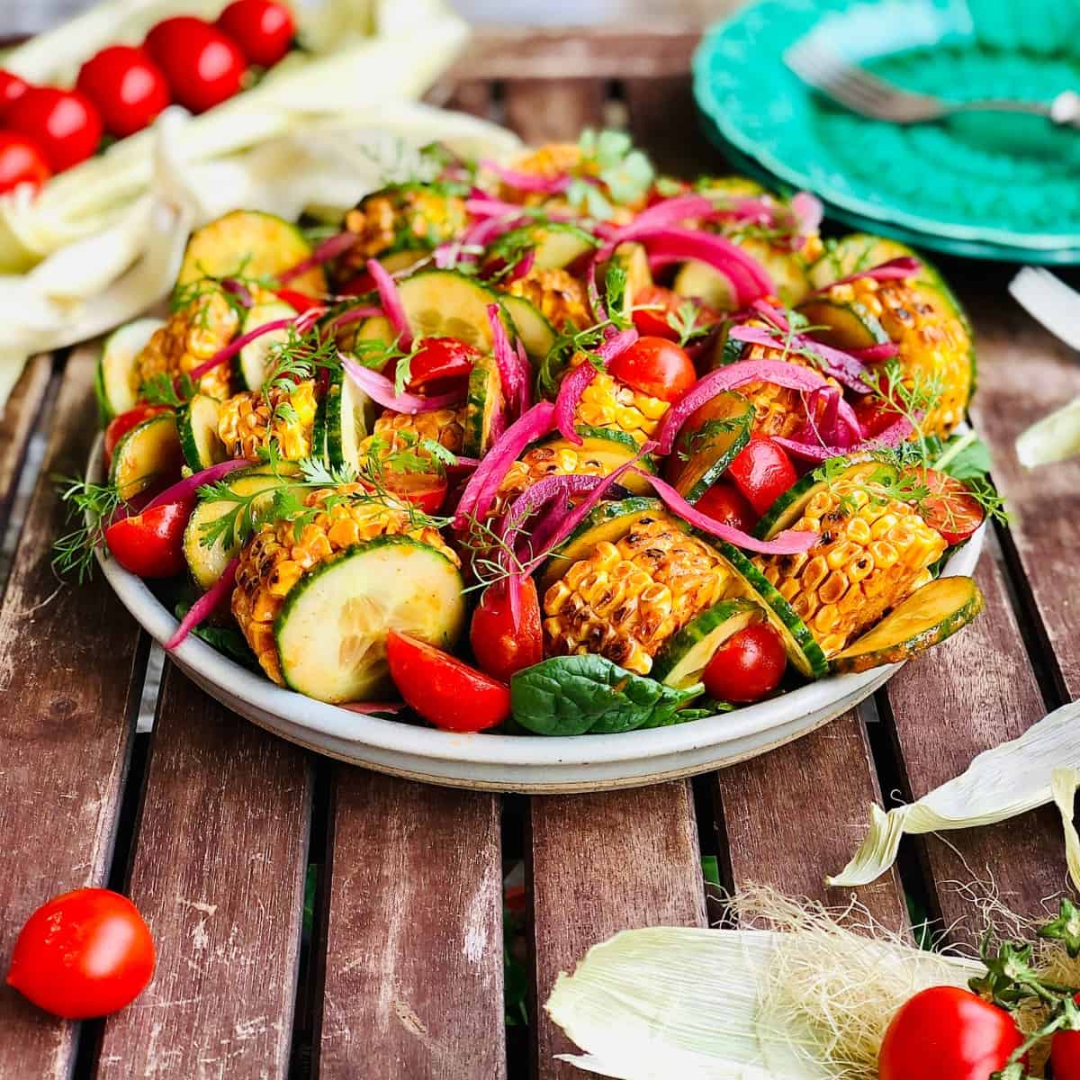 A plate of grilled sweetcorn salad with cucumber and tomato and pickled onion.
