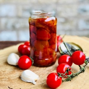 A Jar of confit tomatoes in oil. Surrounded by tomatoes and garlic cloves