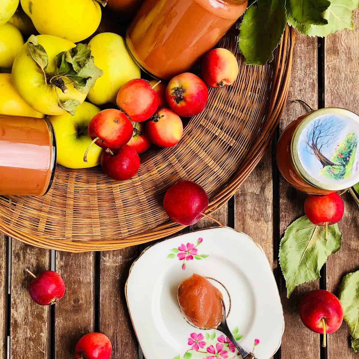 A basket containing apples and jars of crab apple butter, and a small plate with a teaspoon containing apple butter.