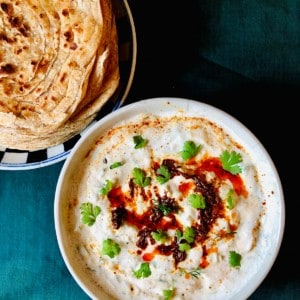 A bowl of cucumber raita and a plate of flat bread.