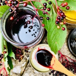 A jar of elderberry syrup with a small wooden spoon containing the elderberry syrup