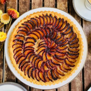 A whole plum tart on a plate sat on a wooden slatted table