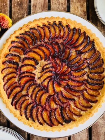 A whole plum tart on a plate sat on a wooden slatted table