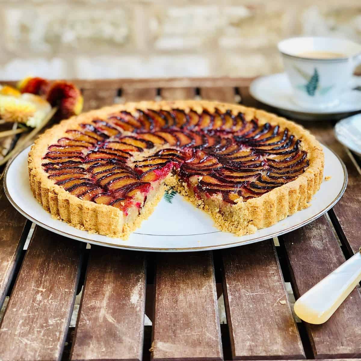 A whole plum tart on a plate sat on a wooden slatted table