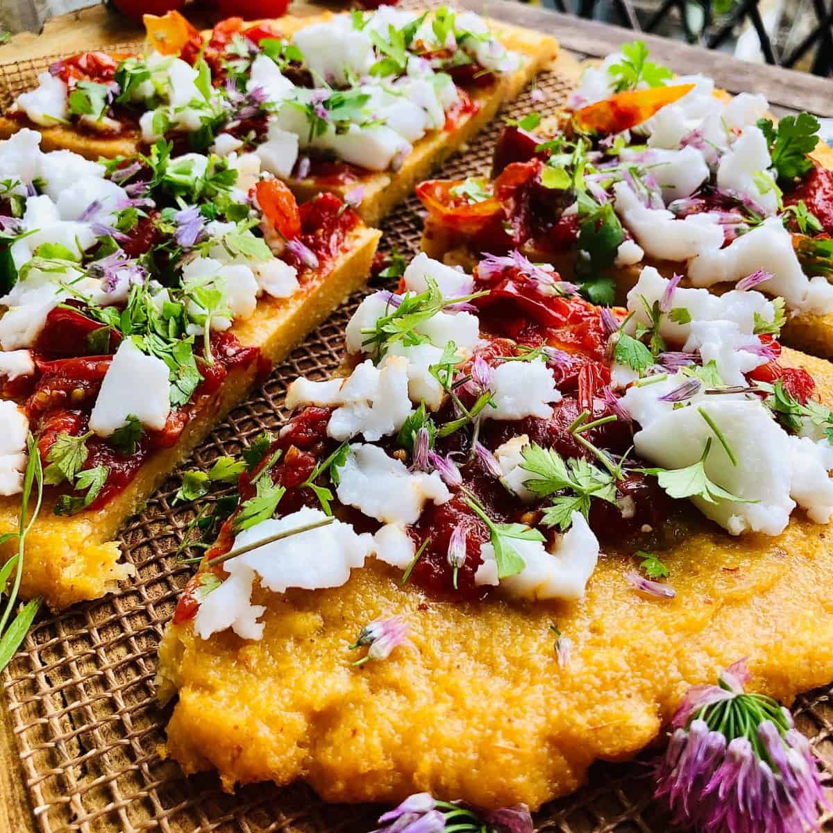 Close up of four slices of baked polenta topped with confit tomatoes and feta