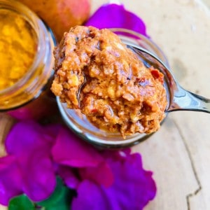 Close up of rose harissa on a teaspoon above two jars of rose harissa