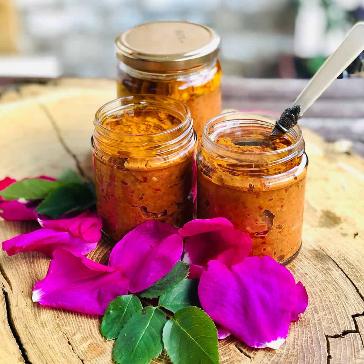 Three jars of rose harissa surrounded by rose petals