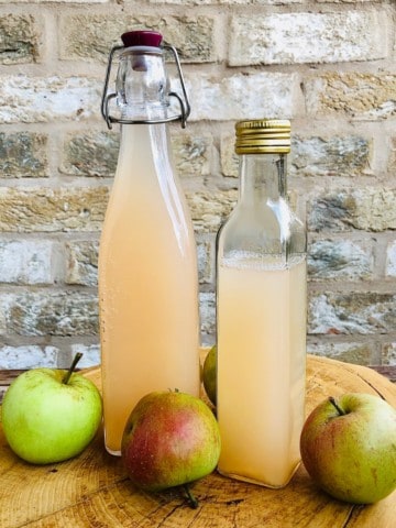 Two bottles of apple cider vinegar sat upon a tree trunk slice platter. 