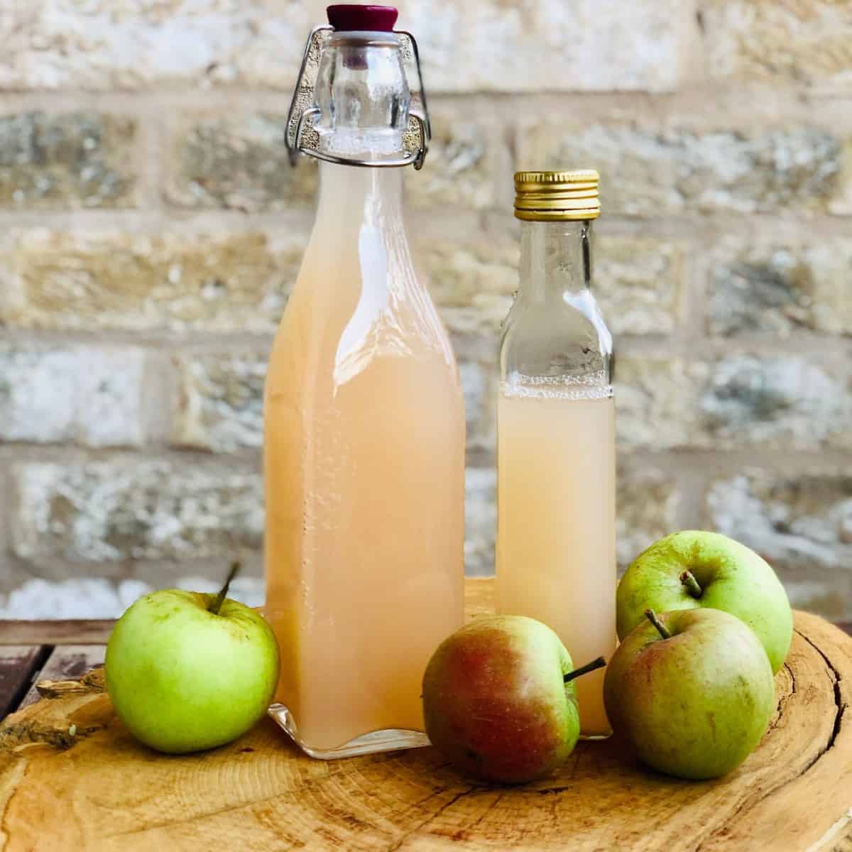 Two bottles of apple cider vinegar sat on a tree trunk slice platter. 
