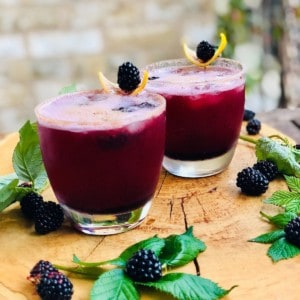 Two glasses of Kala Khatta mocktail garnished with lemon slice and a blackberry.