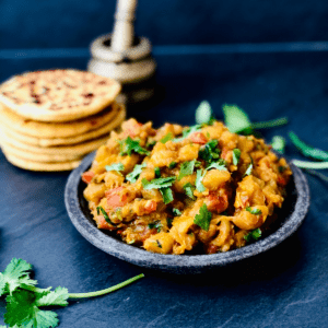 A plate of marrow guhtva garnished with coriander. A plate of flat bread sits in the background