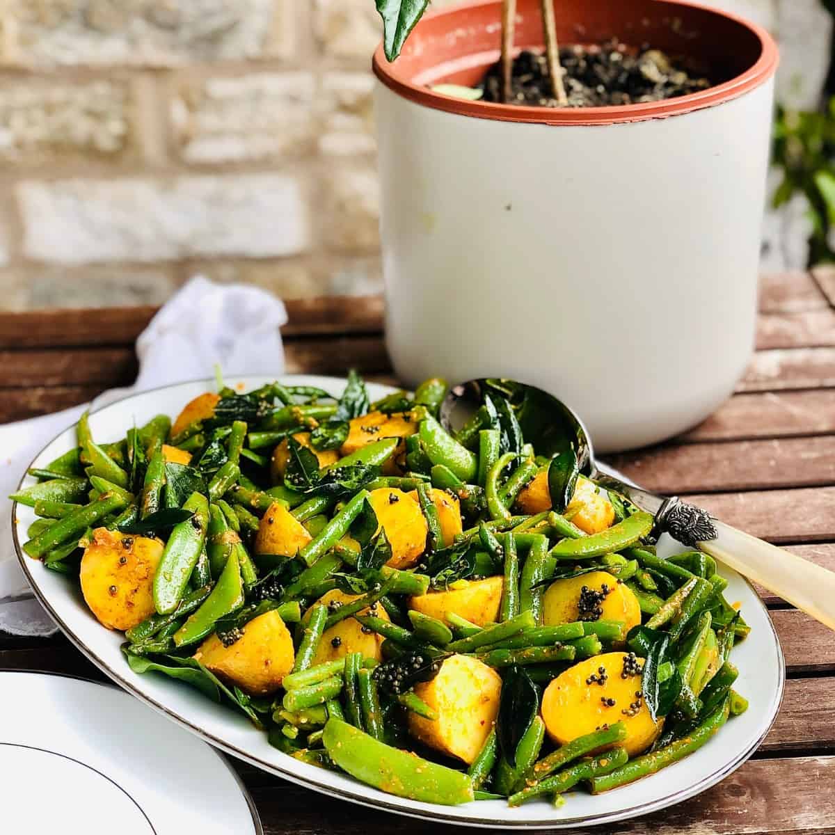 Oval shaped platter of potato and greens salad with an Indian pickle dressing.
