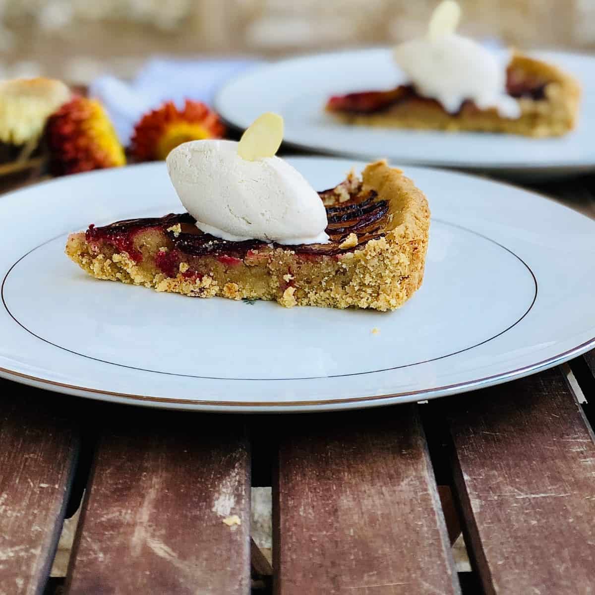 A scoop of dairy free ice cream on top of a slice of plumb tart sat on a small plate