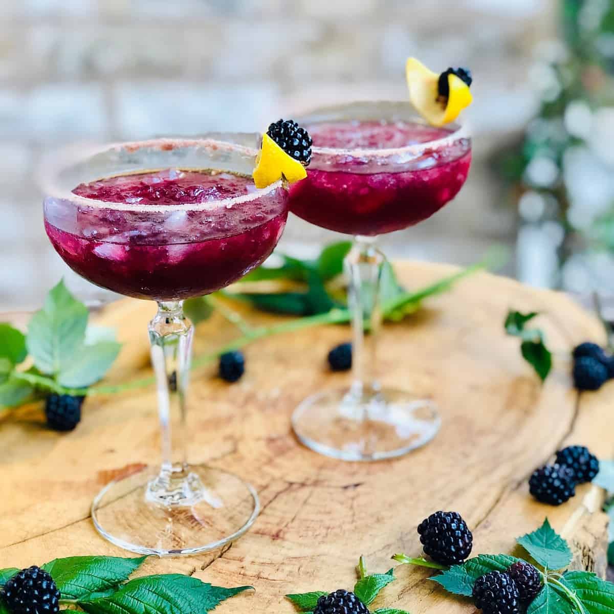 Two margarita glasses containing wild blackberry margarita cocktail. 