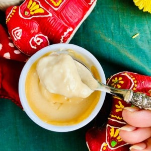 A small pot of bhapa doi Indian dessert. A spoon containing a scoop of bhapa doi is help above the pot