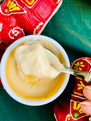 A small pot of bhapa doi Indian dessert. A spoon containing a scoop of bhapa doi is help above the pot