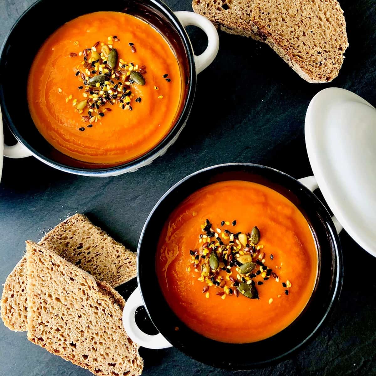 Two bowls of carrot and red pepper soup garnished with seeds. 