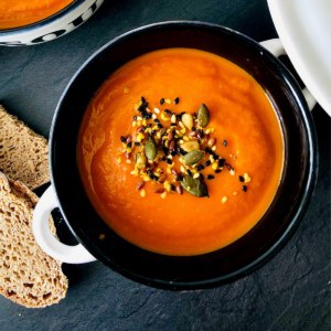 A bowl of carrot and red pepper soup garnished with seeds