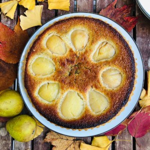 A whole pear tart on a plate sitting on a slatted wooden table. 