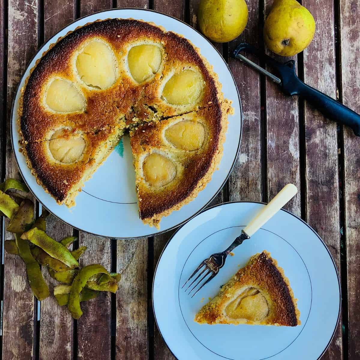 Whole pear tart on a plate with a slice removed. The slice is on a smaller plate.
