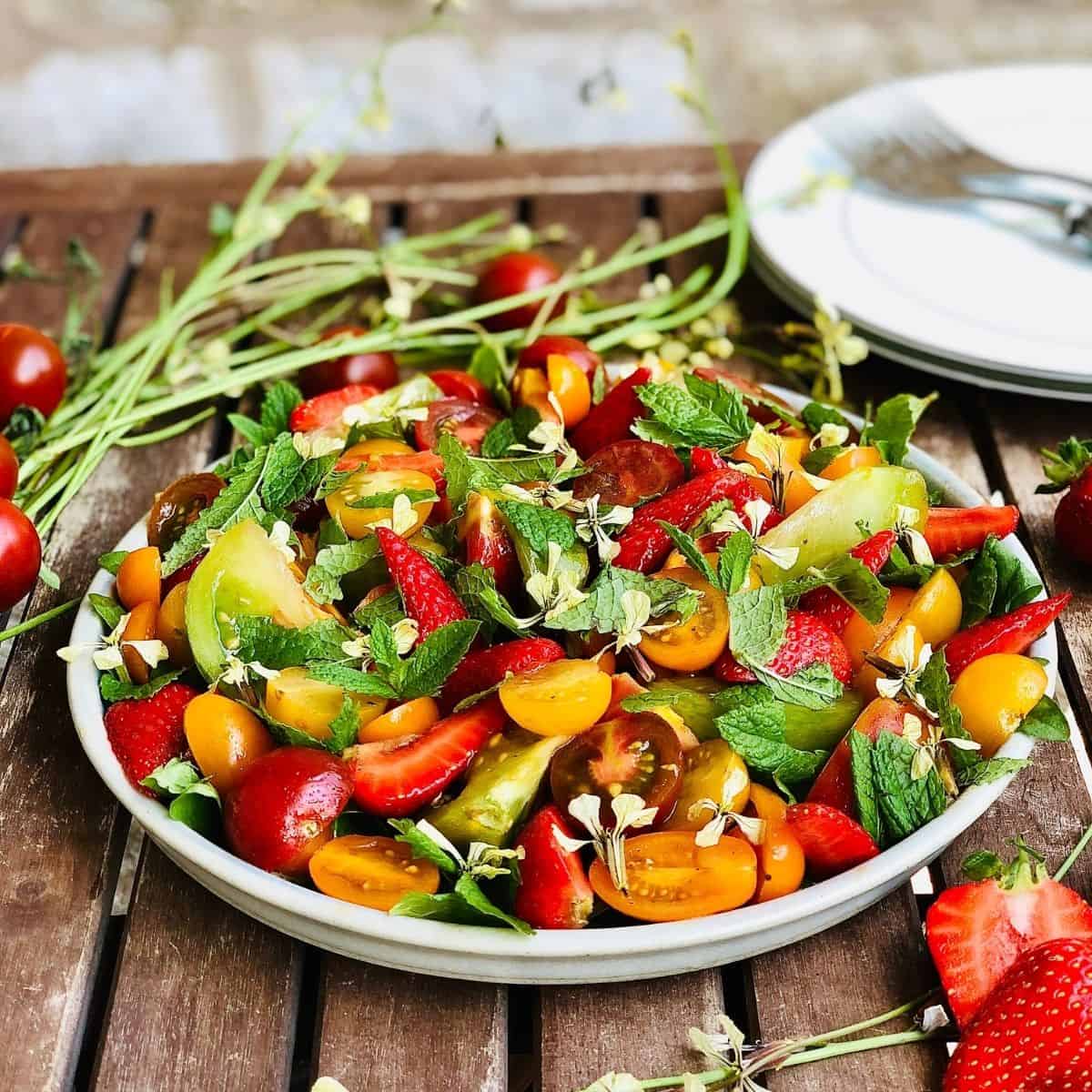 A plate of heirloom tomato and strawberry salad garnished with mint leaves
