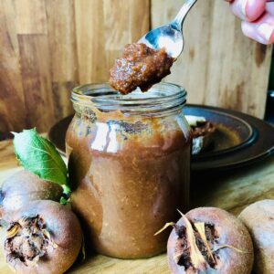 A jar of medlar fruit butter with a spoon resting inside