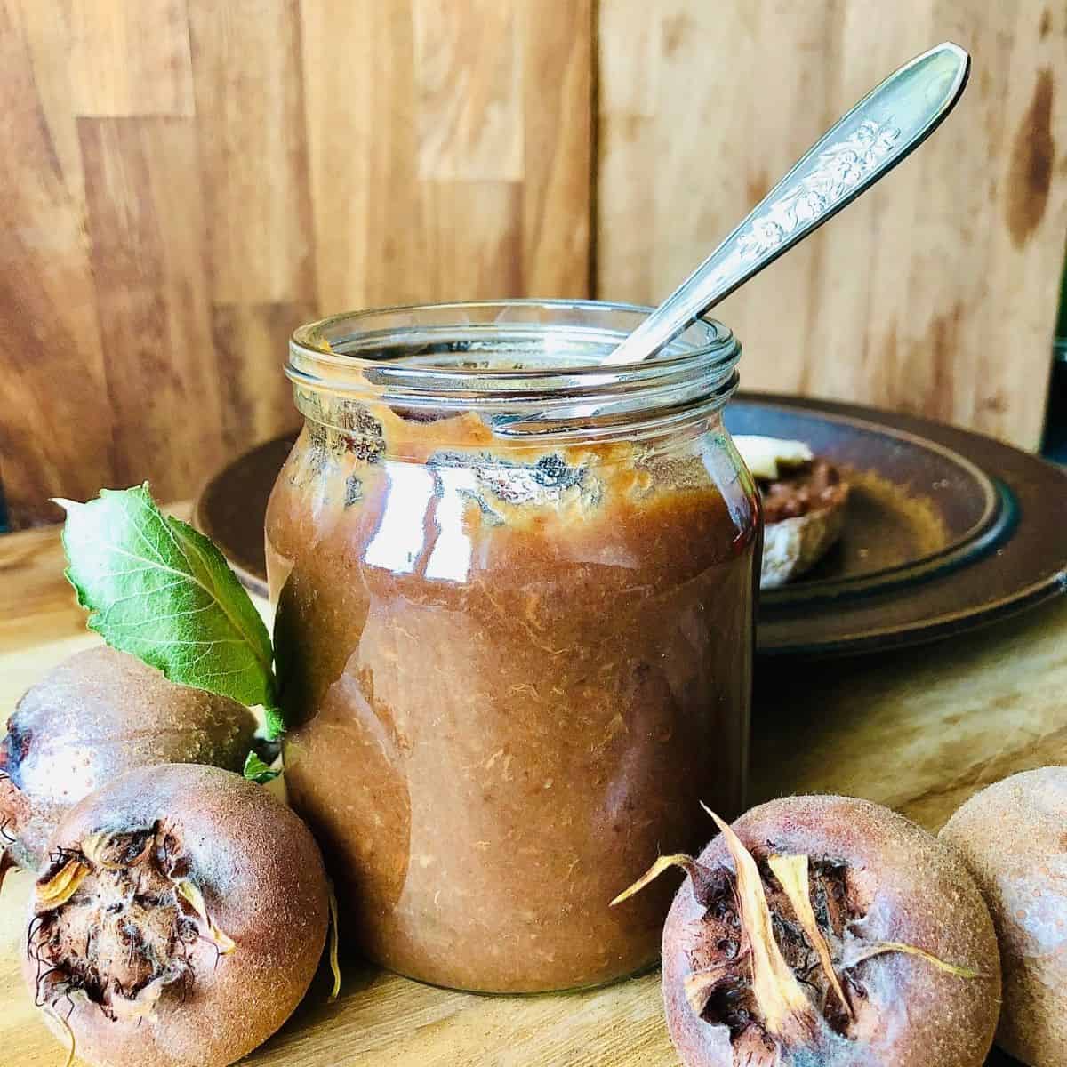 A jar of medlar fruit butter with a spoon resting inside