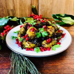 A plate of smashed brussel sprouts with rose Harrisa, garnished with Pomegranate seeds and parsley. 