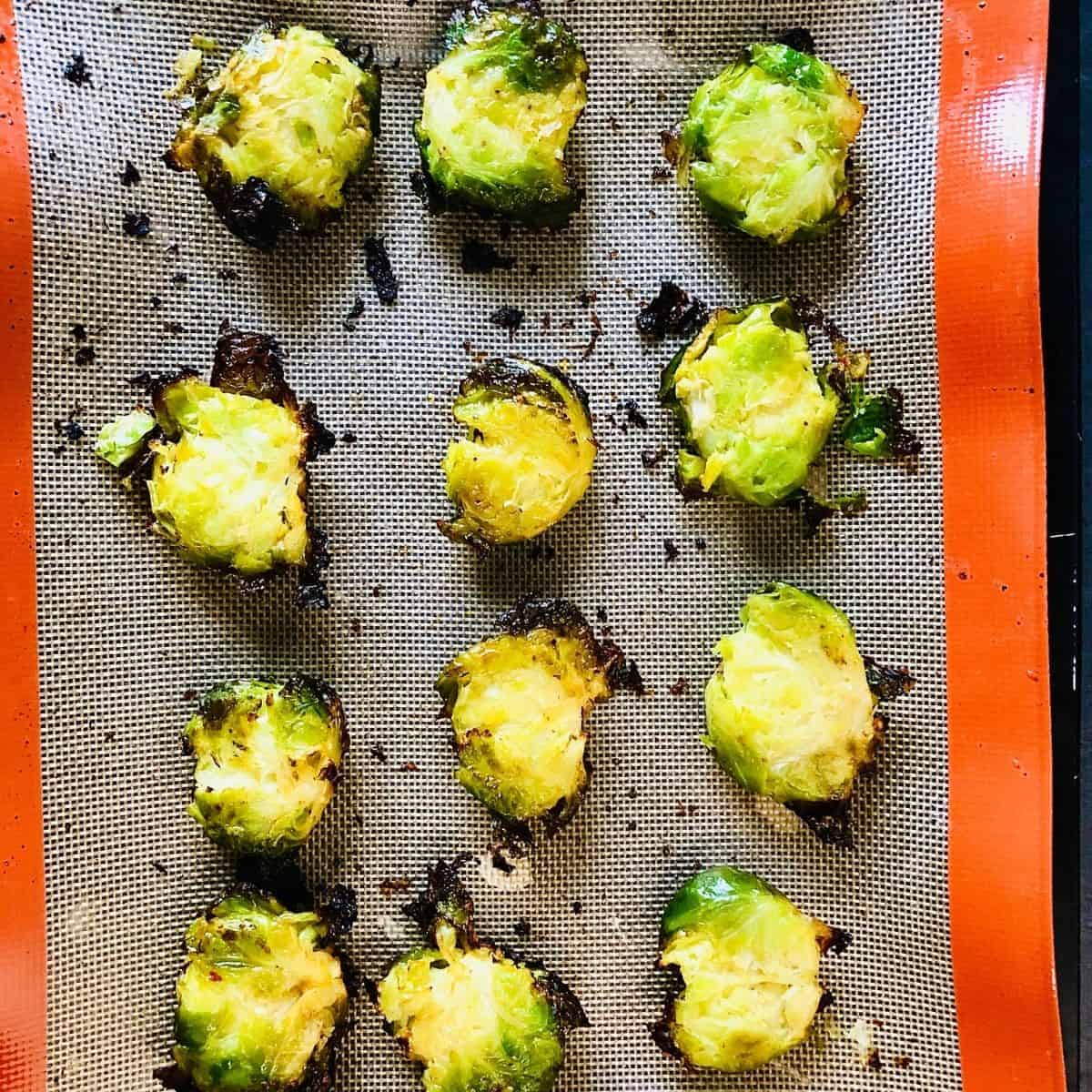 Smashed brussel sprouts in three columns on a silicone mat half way through roasting.
