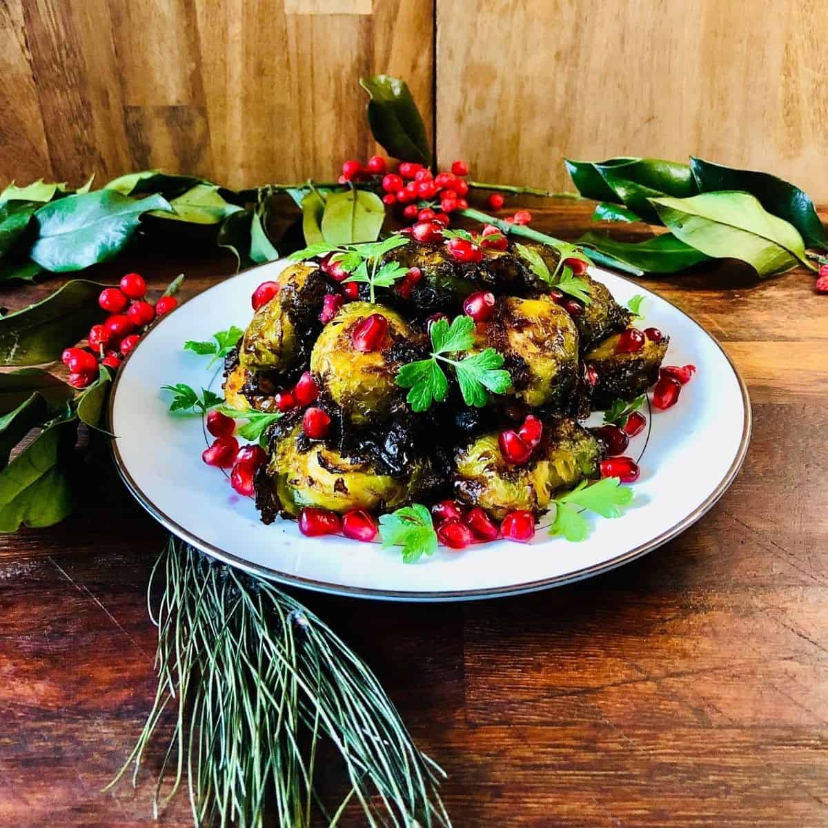 A plate of smashed brussel sprouts with rose Harrisa, garnished with Pomegranate seeds and parsley.
