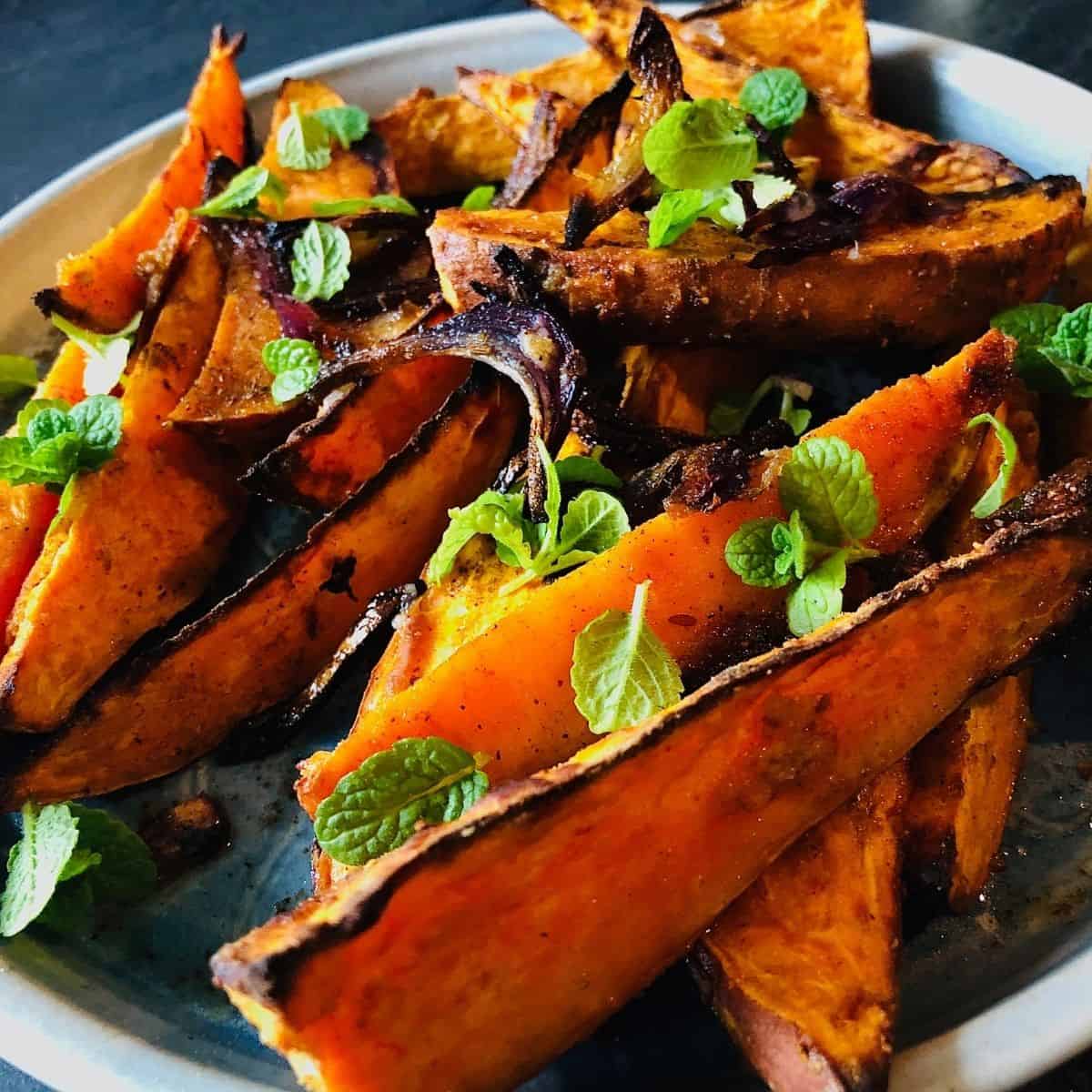 A plate of spiced roasted sweet potato wedges garnished with mint leaves
