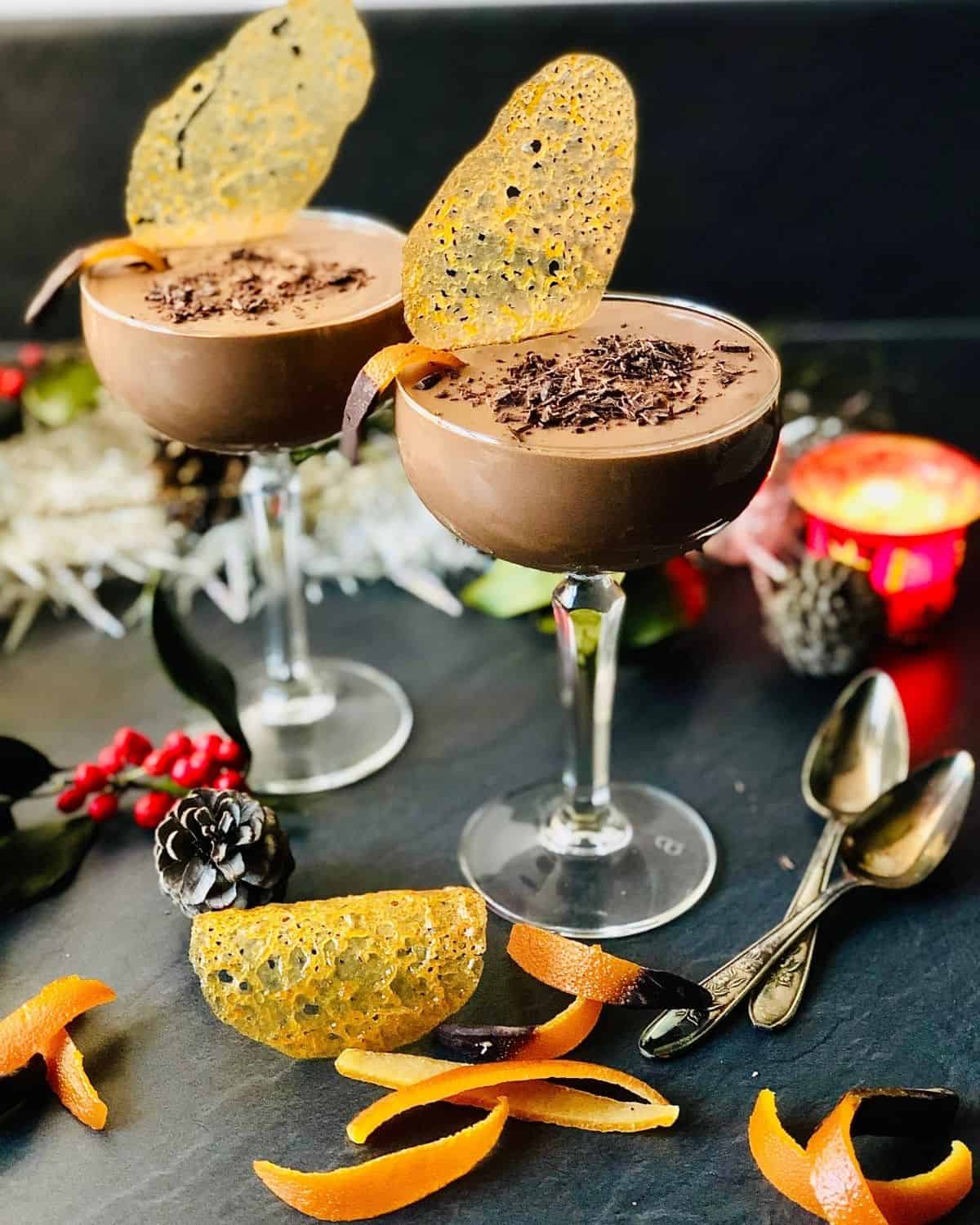 Two Champagne glasses containing vegan chocolate mousse garnished with shaved chocolate and brandy snaps