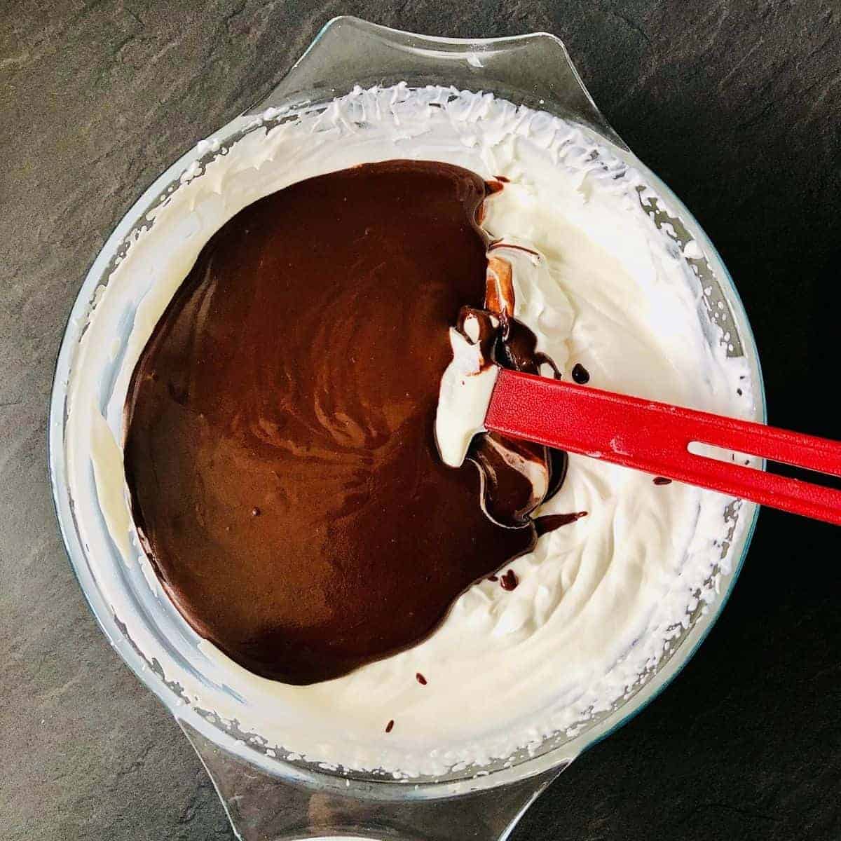 A glass bowl containing melted chocolate and whipped cream, ready to mix