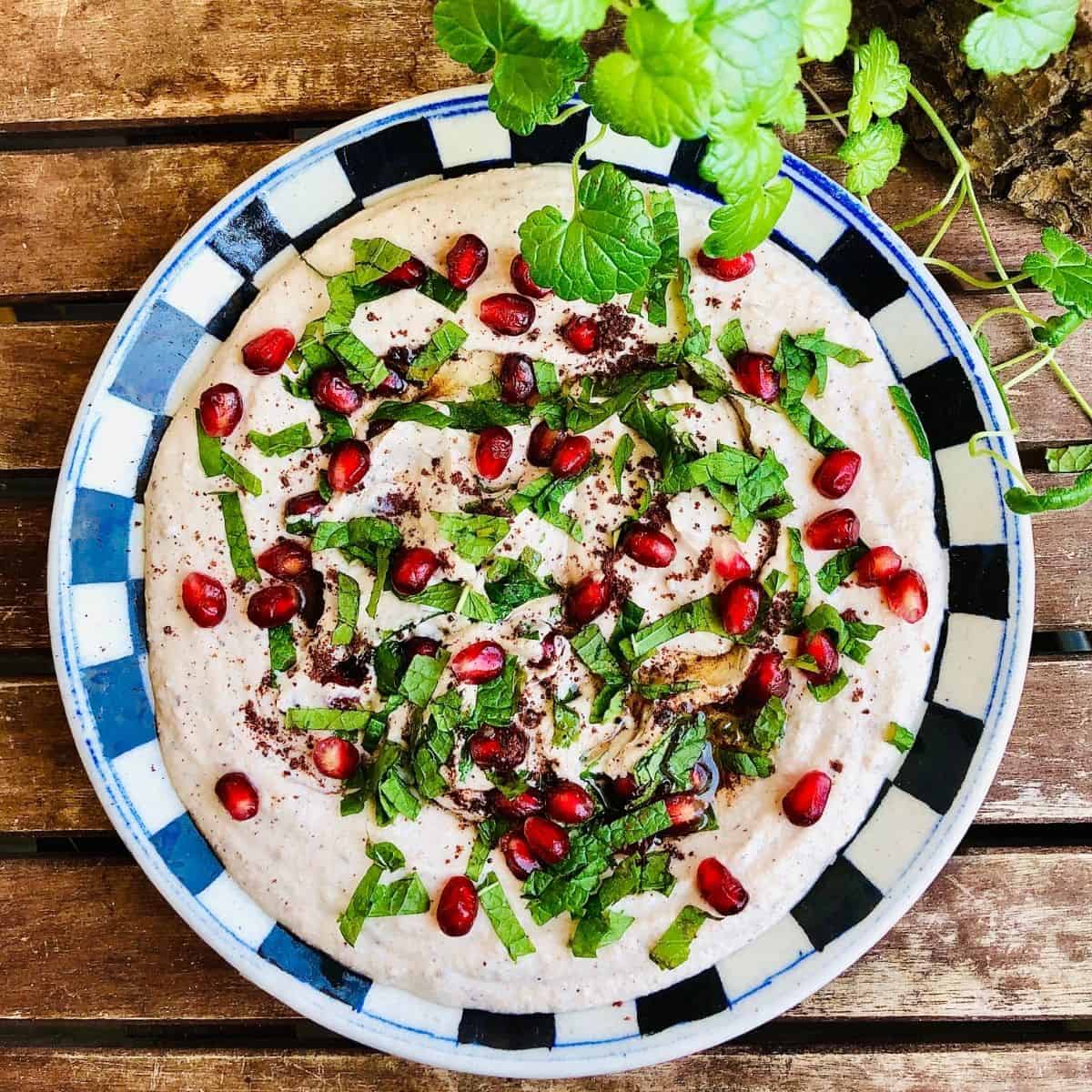 Black eyed pea hummus on a plate garnished with sumac, mint leaves and pomegranate seeds