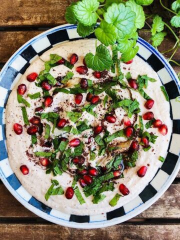 Black eyed pea hummus on a plate garnished with sumac, mint leaves and pomegranate seeds