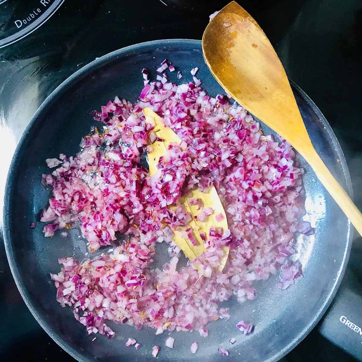 Finely chopped onion and bay leaf for palak paneer cooking in a frying pan