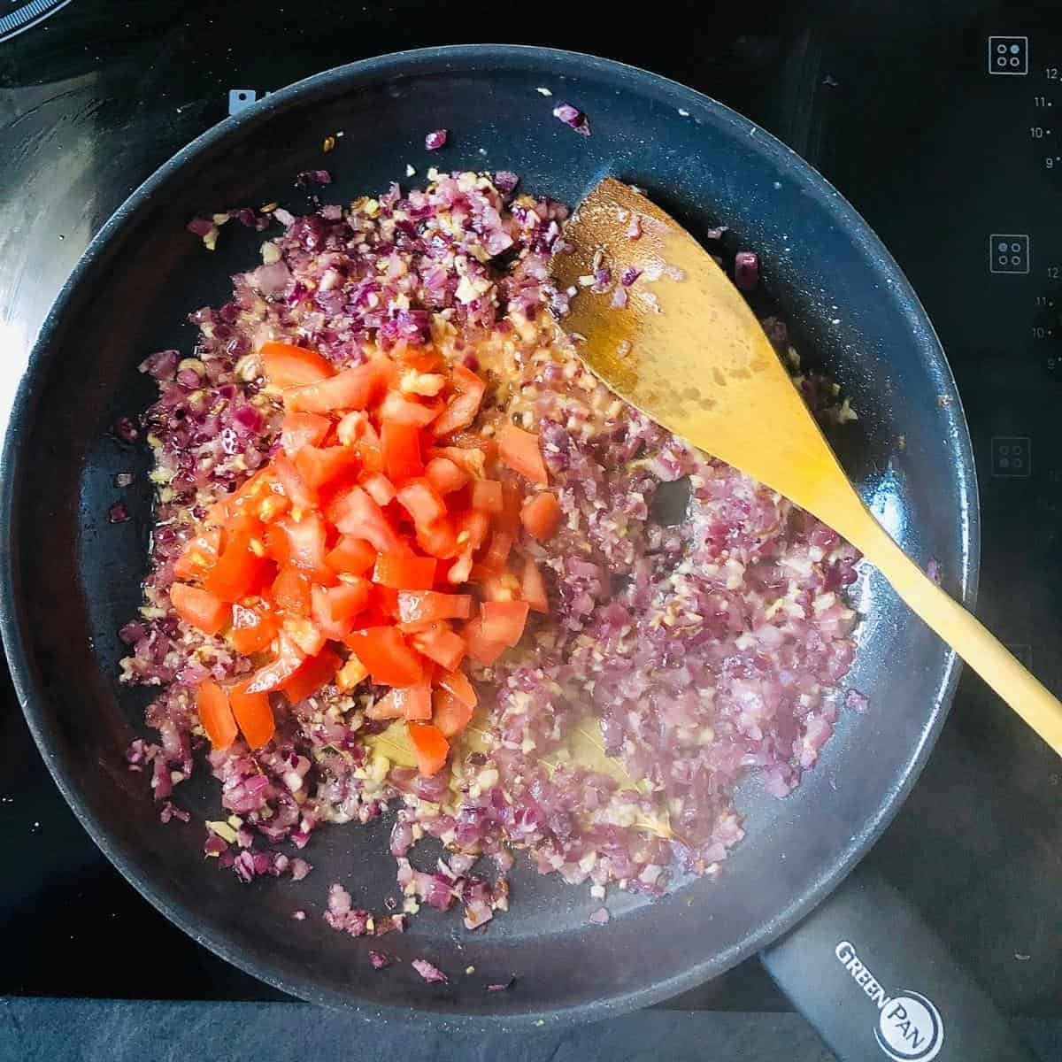 Chopped tomato added to finely chopped onion, garlic and ginger cooking  in a frying pan