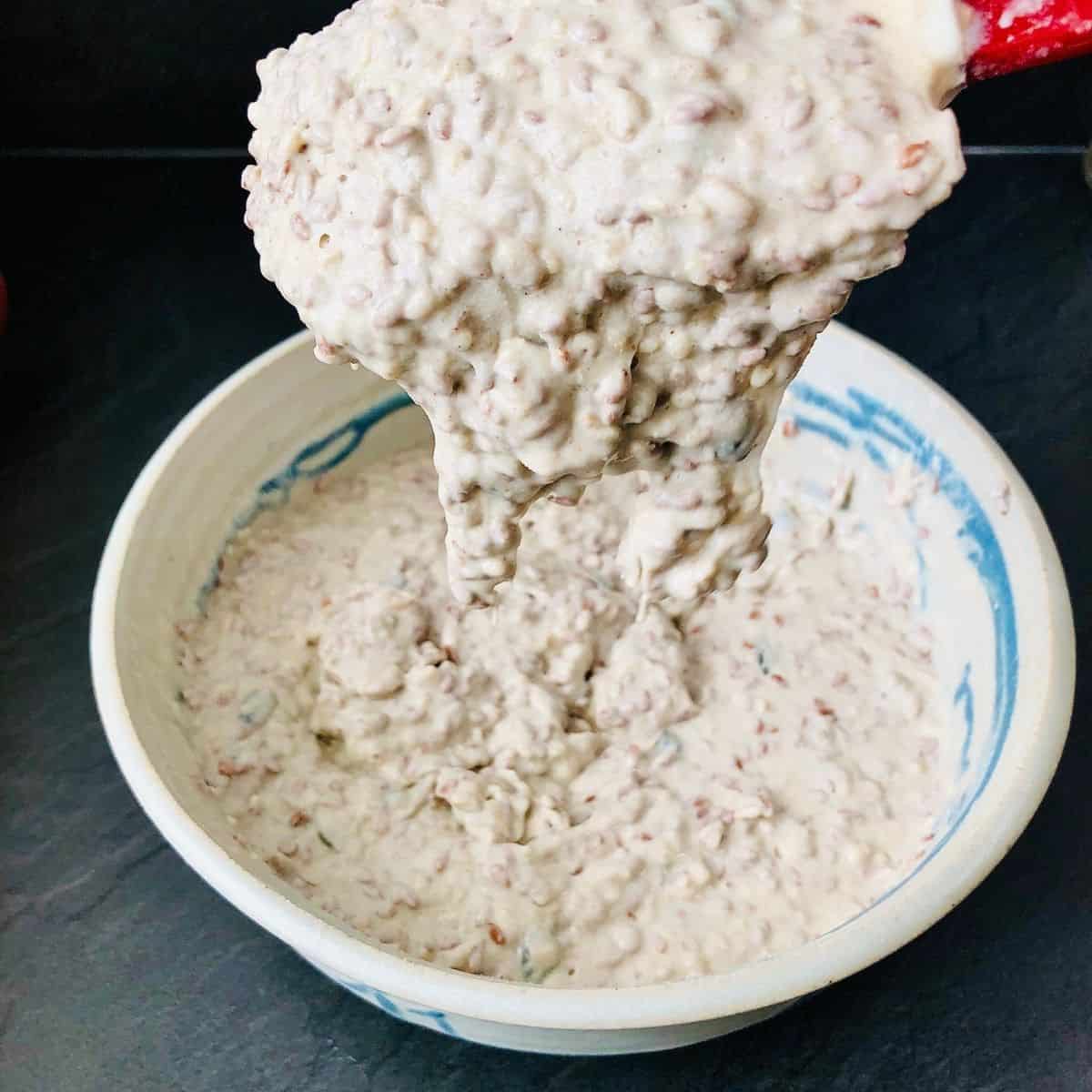 Wet cracker dough mix falling off a spatula into a bowl of wet cracker dough, showing consistency
