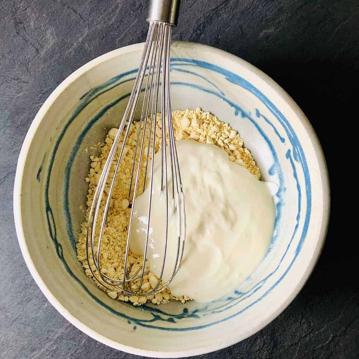 A bowl of gram flour and yoghurt and a whisk
