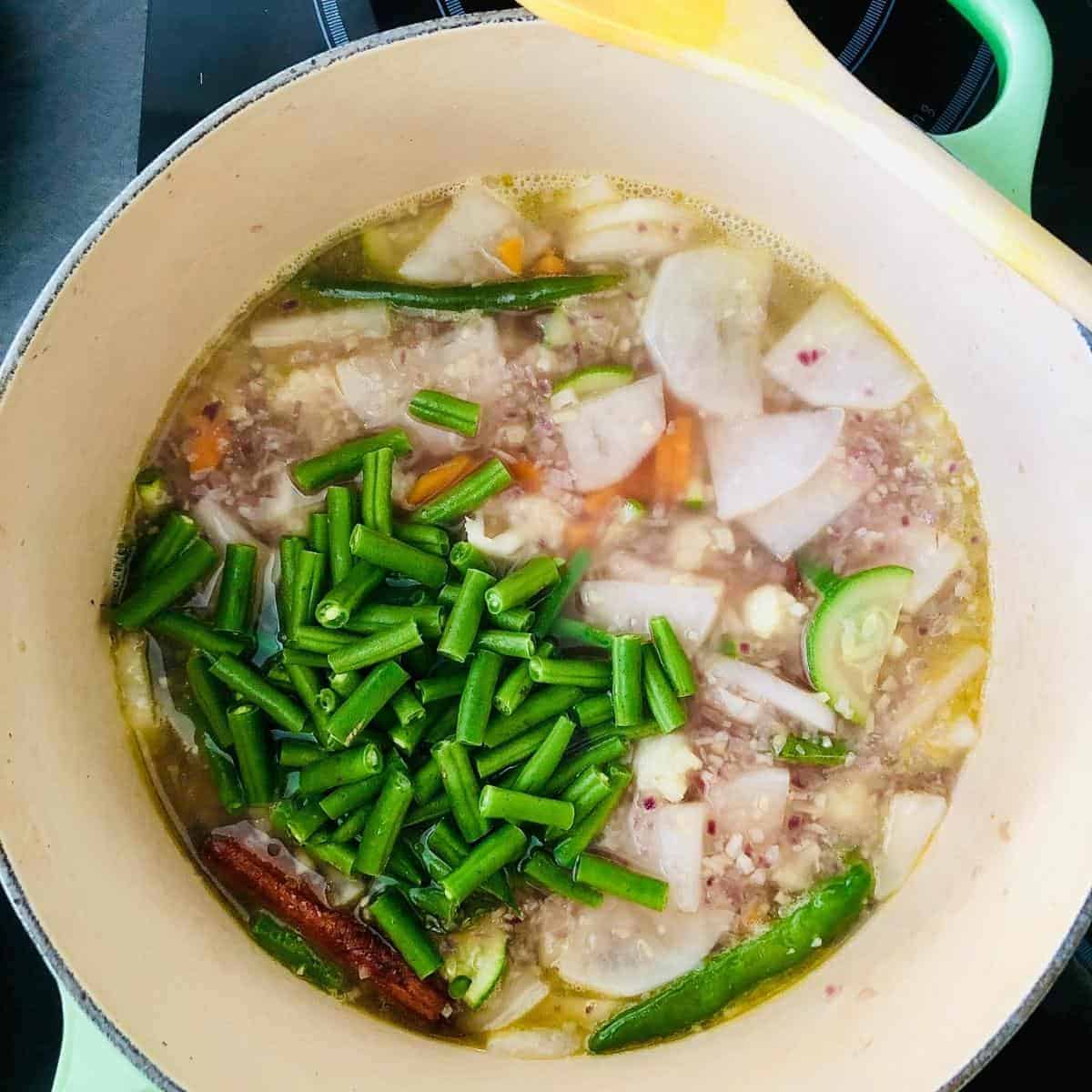 Green beans added to ishtew vegetable stew in a pot for further cooking
