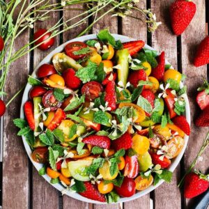 A plate of heirloom tomato and strawberry salad garnished with mint leaves