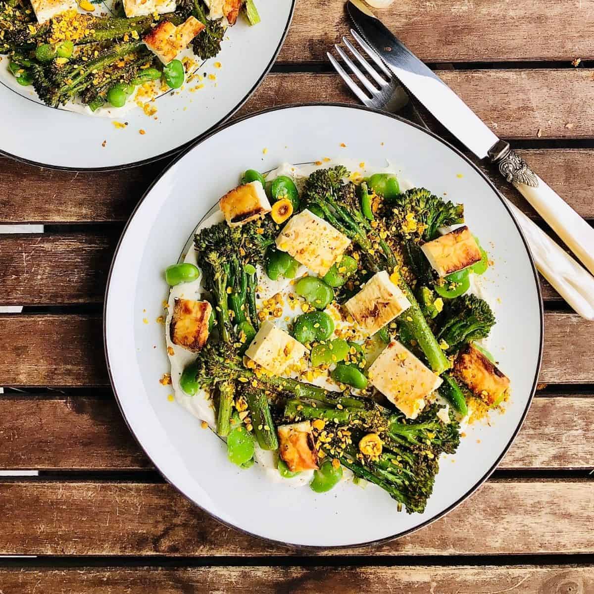 A plate of labnah with grilled broccoli and baked feta on a slatted wooden table