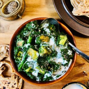 A shallow dish containing palak paneer garnished with vegan cream