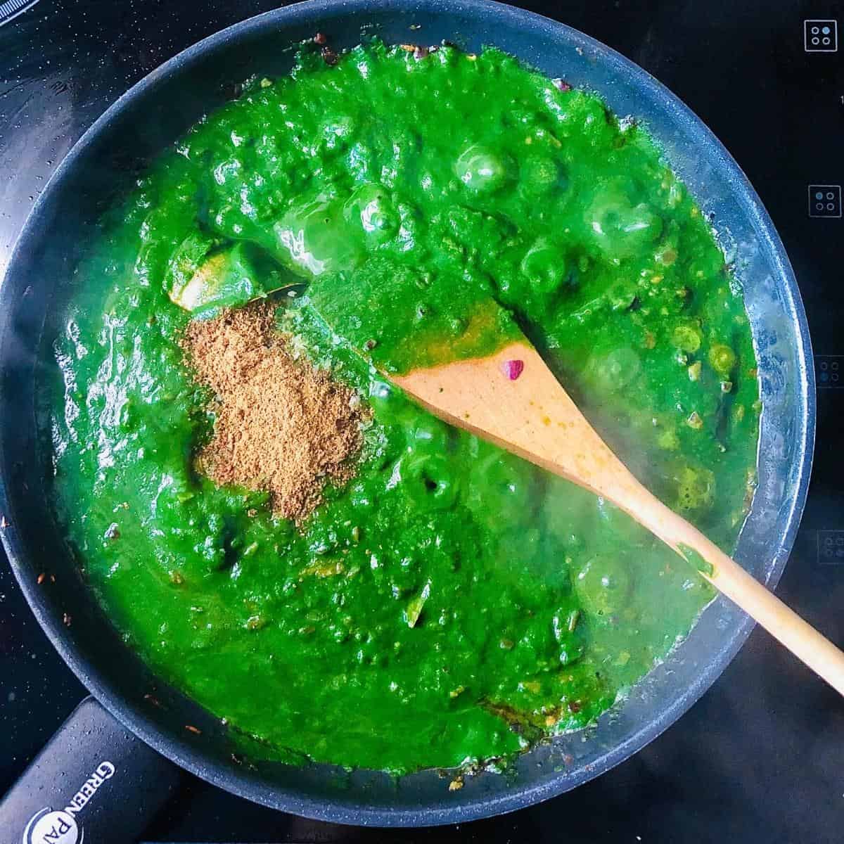 Spinach puree mixed into palak paneer base mix and gram masala added in a frying pan