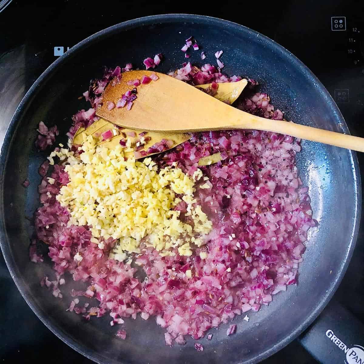 Finely chopped garlic and ginger added to finely chopped onion cooking in a frying pan
