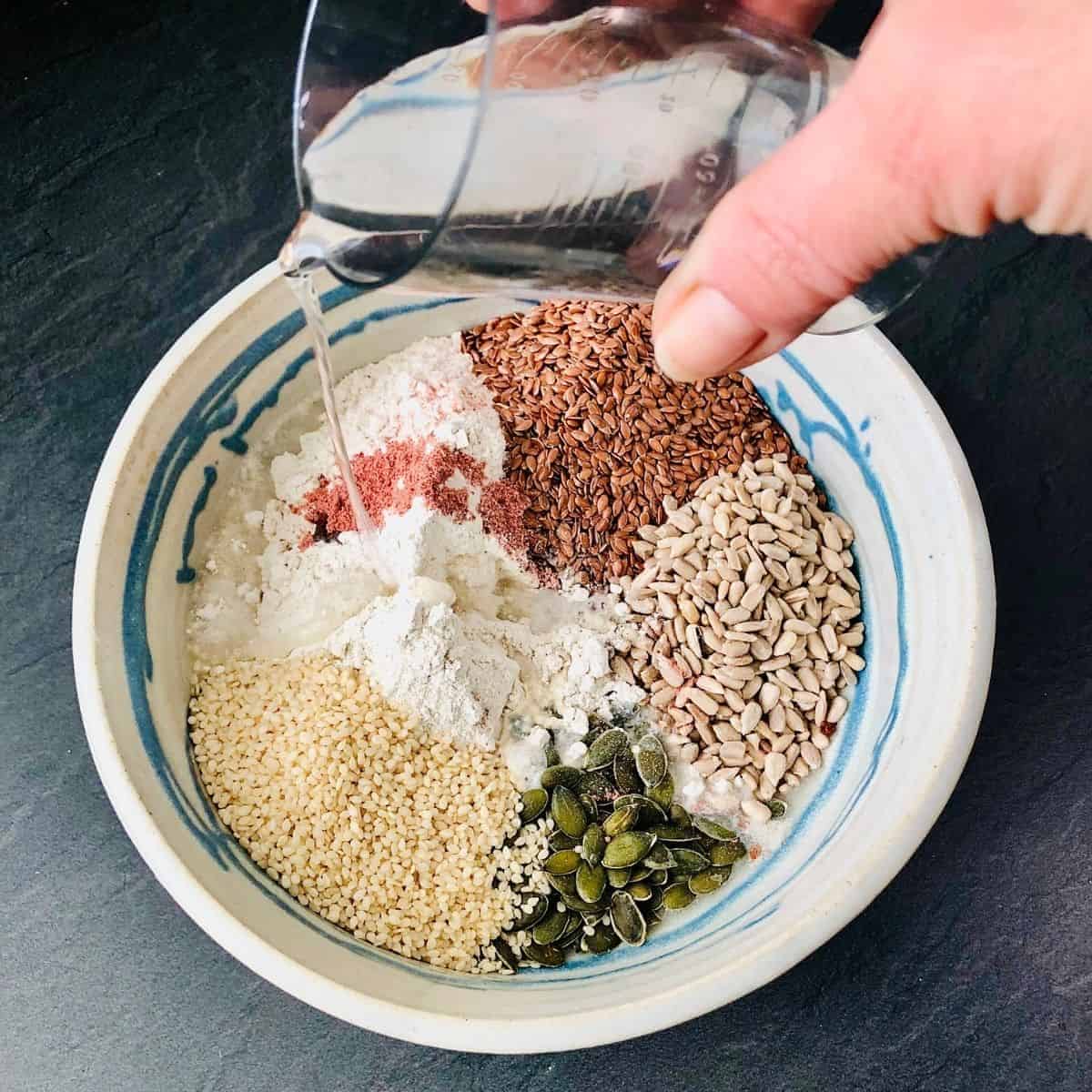 Adding water to dry cracker ingredients in a bowl
