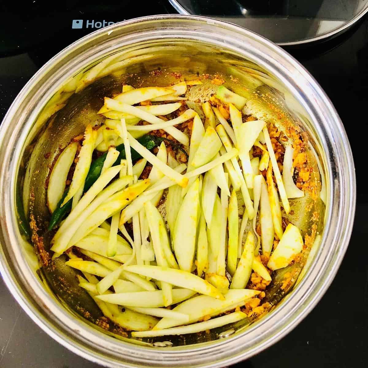 Adding raw mango to a saucepan on a stove for charchari mixed vegetable recipe